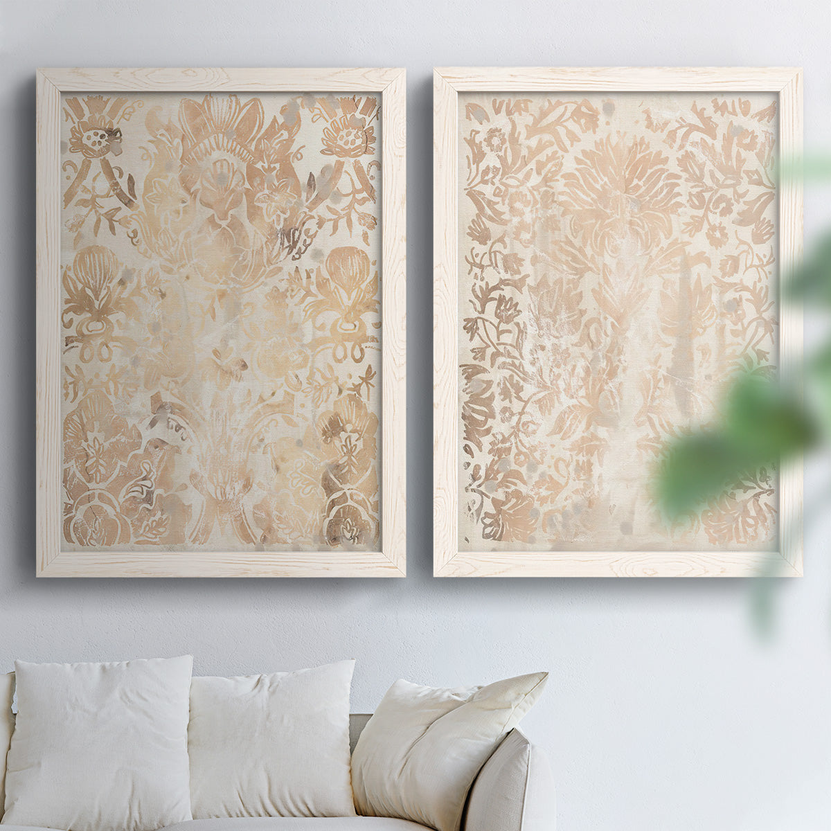 Set of two white barnwood framed canvas prints depicting dense scrolling foliage, distressed walnut-brown texture, and symmetrical motifs arranged across two complementary compositions above a sofa in a bright living space.