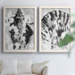 Set of two white barnwood framed canvas prints depicting radiating splashes, mirrored organic forms, and watery bleed textures arranged across two complementary compositions above a sofa in a bright living space.