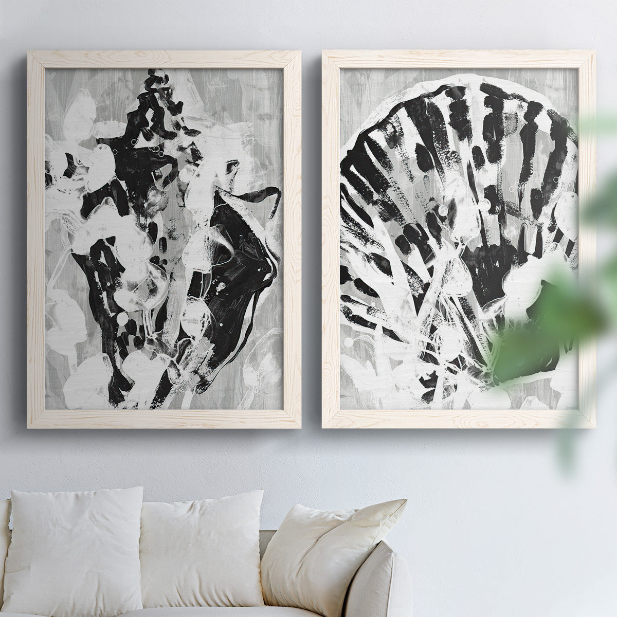 Set of two white barnwood framed canvas prints depicting radiating splashes, mirrored organic forms, and watery bleed textures arranged across two complementary compositions above a sofa in a bright living space.