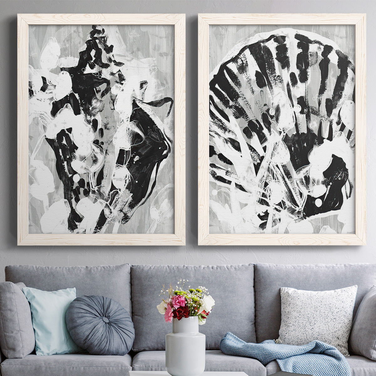 Set of two white barnwood framed canvas prints depicting paired dramatic monochrome abstracts with radiating splashes, mirrored organic forms, and watery bleed textures above a sofa in a contemporary living room.