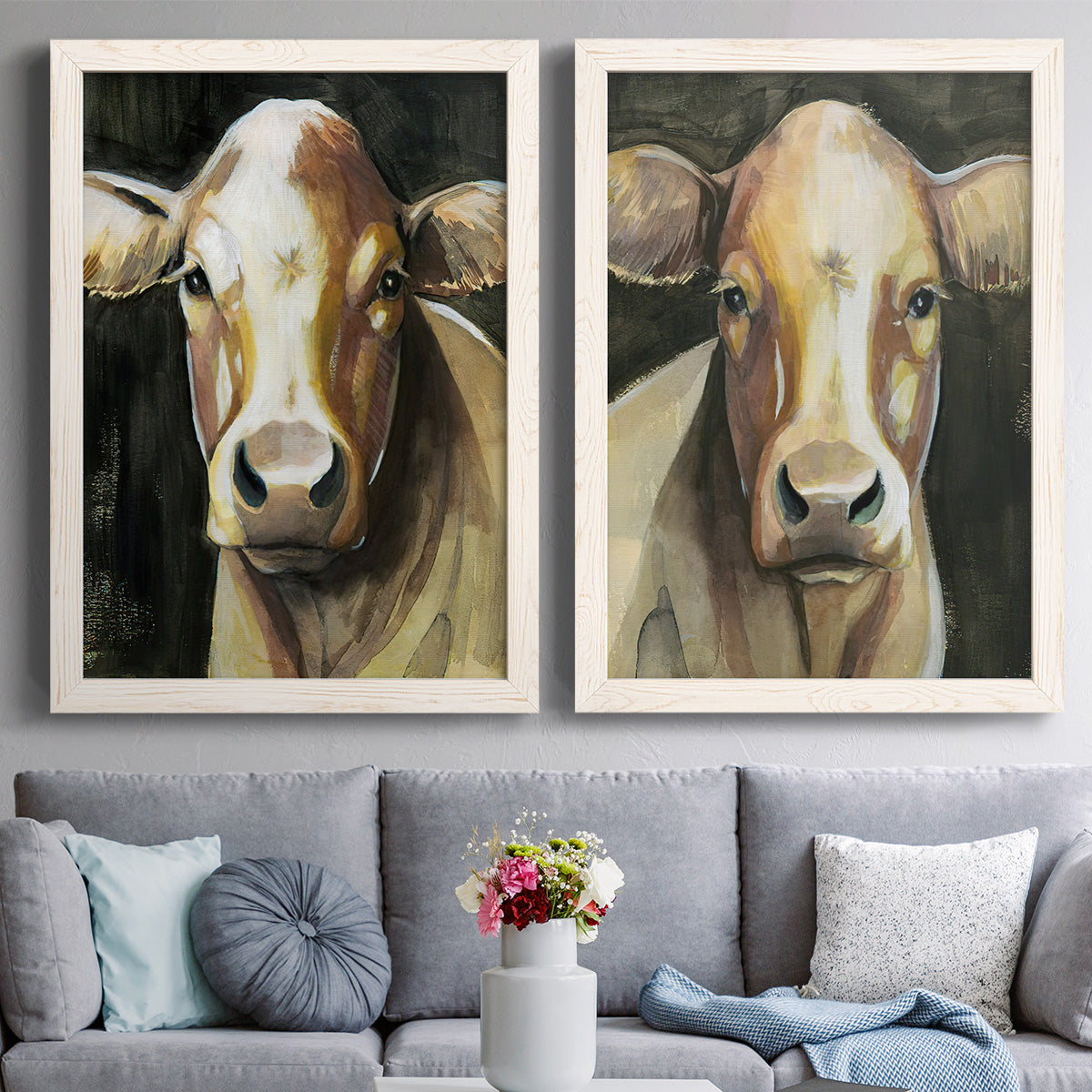 Set of two white barnwood framed canvas prints depicting paired painterly farm-animal portraits with large expressive eyes, warm brown faces, and dark backgrounds above a sofa in a contemporary living room.