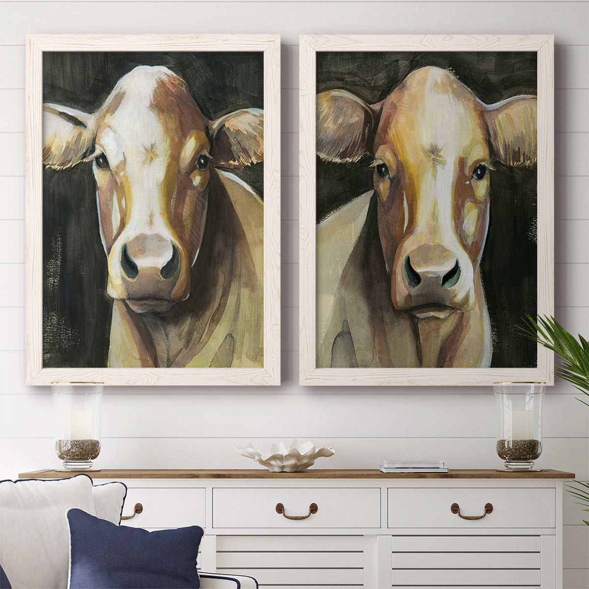 Set of two white barnwood framed canvas prints depicting a coordinated art pair of close-up portraits of gentle brown cows rendered as painterly farm-animal portraits above a dining room sideboard.