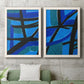 Set of two white barnwood framed canvas prints depicting a coordinated art pair of intersecting black bars over vivid blue fields rendered as bold geometric abstracts above a sofa in a modern living room.