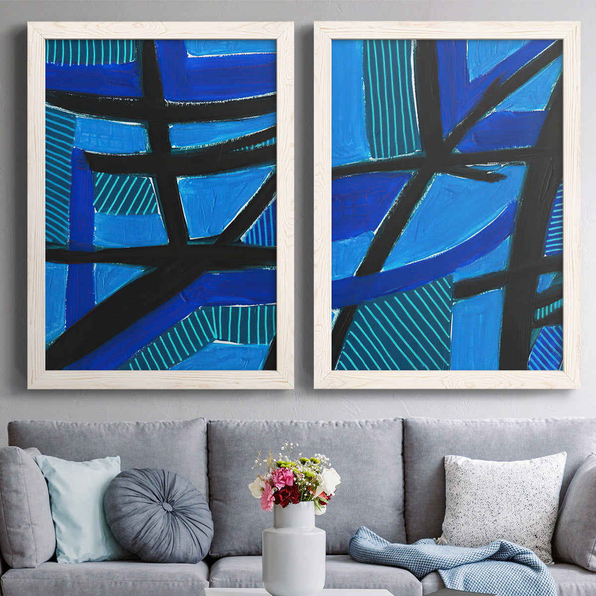 Set of two white barnwood framed canvas prints depicting paired bold geometric abstracts with cobalt turquoise and navy sections with strong diagonal structure above a sofa in a contemporary living room.