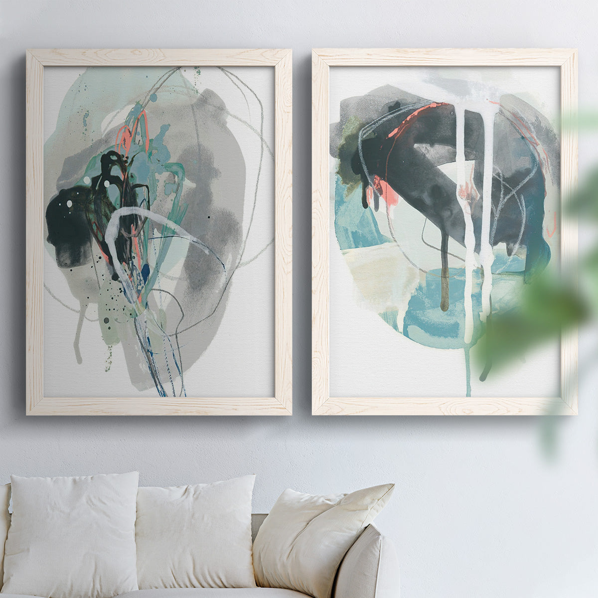 Set of two white barnwood framed canvas prints depicting looping ink forms, drips, pale washes, and coral accents arranged across two complementary compositions above a sofa in a bright living space.