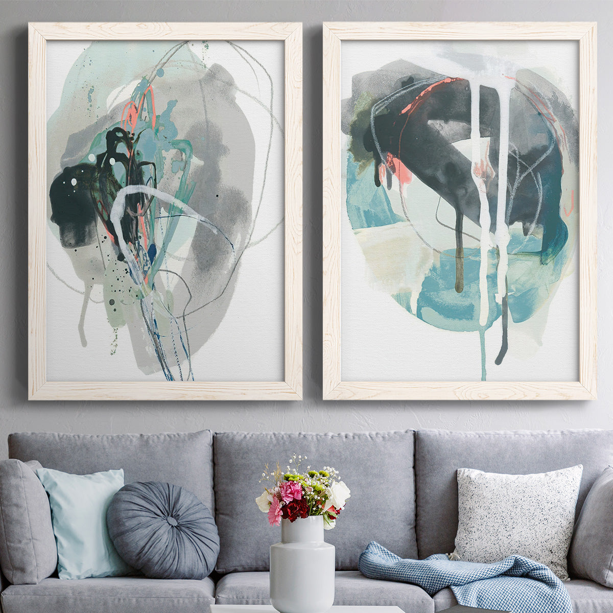 Set of two white barnwood framed canvas prints depicting paired bold gestural abstracts with looping ink forms, drips, pale washes, and coral accents above a sofa in a contemporary living room.