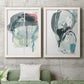 Set of two white barnwood framed canvas prints depicting a coordinated art pair of large black gray and teal circular gestures rendered as bold gestural abstracts above a sofa in a modern living room.