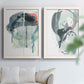 Set of two white barnwood framed canvas prints depicting looping ink forms, drips, pale washes, and coral accents arranged across two complementary compositions above a sofa in a bright living space.