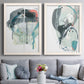 Set of two white barnwood framed canvas prints depicting paired bold gestural abstracts with looping ink forms, drips, pale washes, and coral accents above a sofa in a contemporary living room.