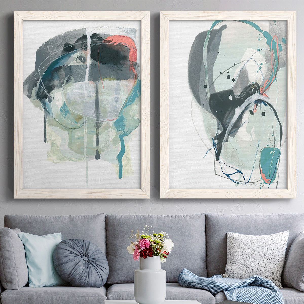 Set of two white barnwood framed canvas prints depicting paired bold gestural abstracts with looping ink forms, drips, pale washes, and coral accents above a sofa in a contemporary living room.