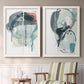 Set of two white barnwood framed canvas prints depicting two bold gestural abstracts featuring large black gray and teal circular gestures above a sideboard in a cozy sitting room.