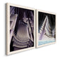 Angled view of a set of two white barnwood framed canvas prints featuring two vintage architectural illustrations featuring dramatic Art Deco city and theater scenes.