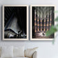 Set of two white barnwood framed canvas prints depicting monumental skyscrapers, sweeping stairways, spotlights, and elegant nighttime figures arranged across two complementary compositions above a sofa in a bright living space.