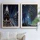 Set of two white barnwood framed canvas prints depicting stylized metropolitan scenes featuring glowing windows monumental buildings and cinematic blue black skies above a sofa in a bright living space.
