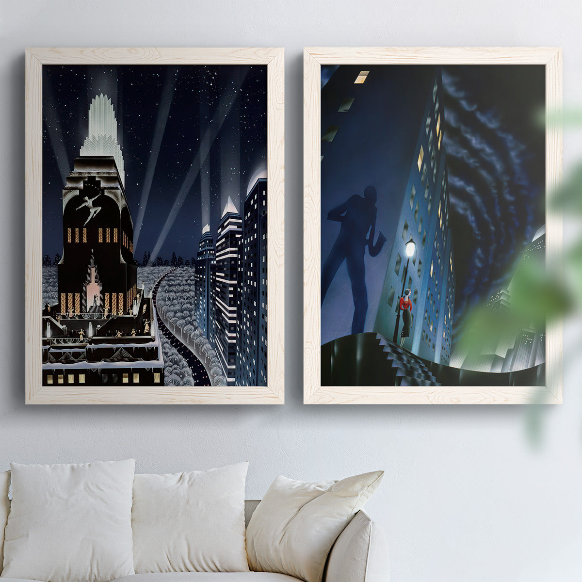 Set of two white barnwood framed canvas prints depicting stylized metropolitan scenes featuring glowing windows monumental buildings and cinematic blue black skies above a sofa in a bright living space.