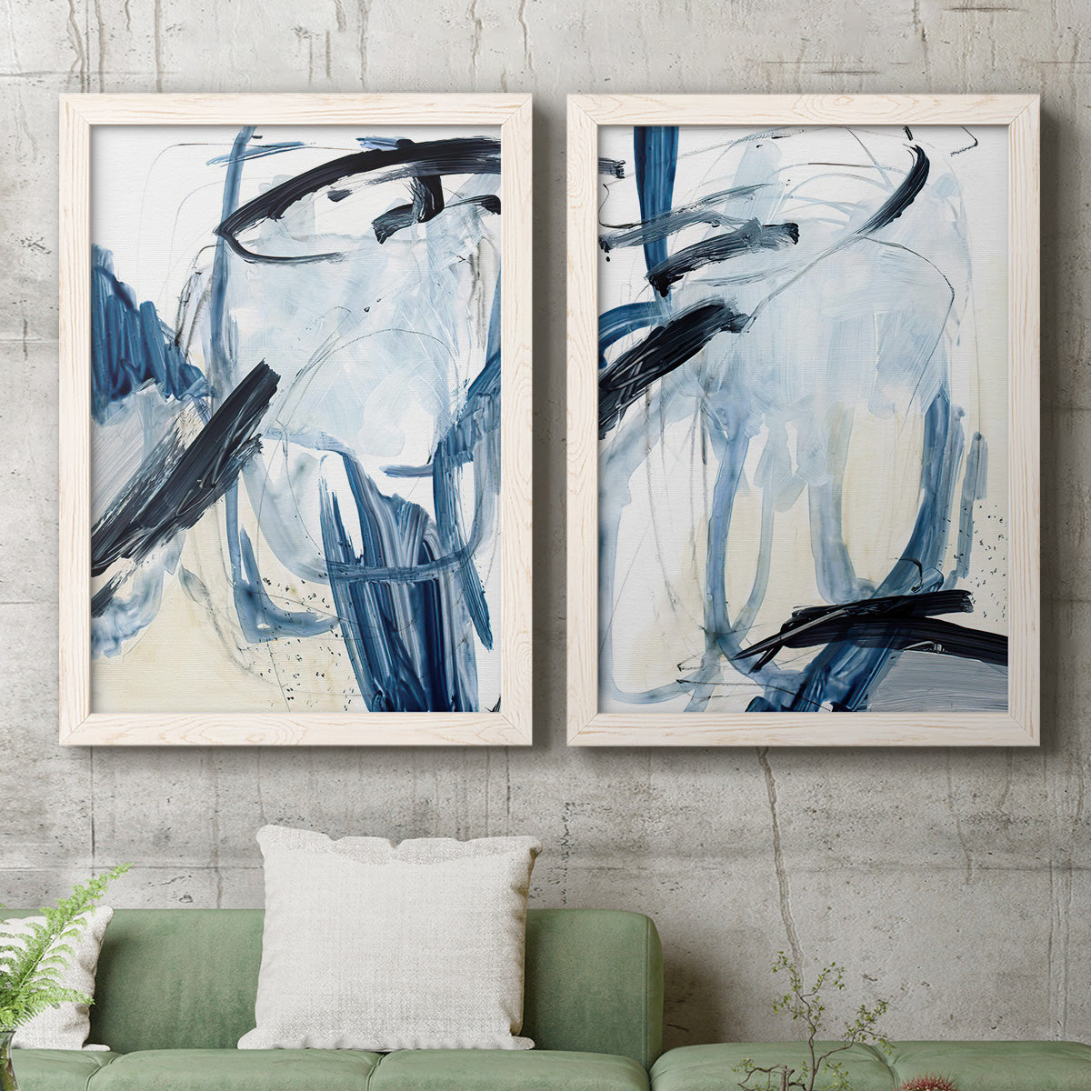 Set of two white barnwood framed canvas prints depicting a coordinated art pair of sweeping indigo and black gestural brushwork rendered as expressive blue abstracts above a sofa in a modern living room.