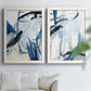 Set of two white barnwood framed canvas prints depicting broad curved strokes, pale washes, and energetic ink lines arranged across two complementary compositions above a sofa in a bright living space.