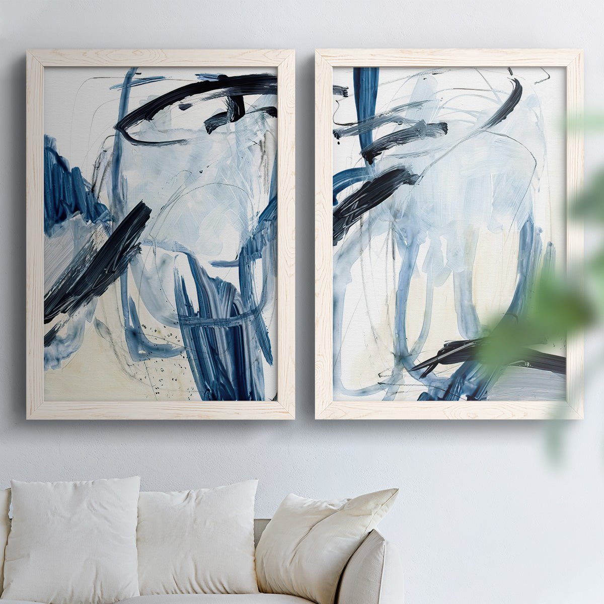 Set of two white barnwood framed canvas prints depicting broad curved strokes, pale washes, and energetic ink lines arranged across two complementary compositions above a sofa in a bright living space.