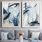 Set of two white barnwood framed canvas prints depicting paired expressive blue abstracts with broad curved strokes, pale washes, and energetic ink lines above a sofa in a contemporary living room.