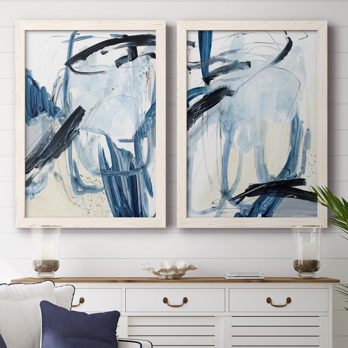 Set of two white barnwood framed canvas prints depicting a coordinated art pair of sweeping indigo and black gestural brushwork rendered as expressive blue abstracts above a dining room sideboard.