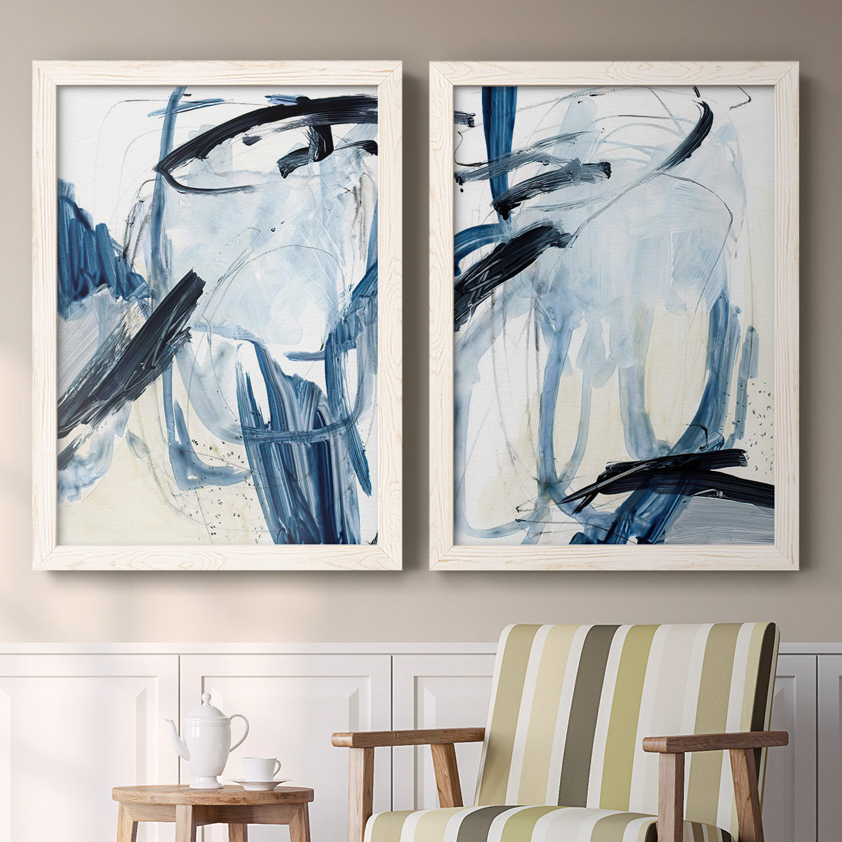 Set of two white barnwood framed canvas prints depicting two expressive blue abstracts featuring sweeping indigo and black gestural brushwork above a sideboard in a cozy sitting room.
