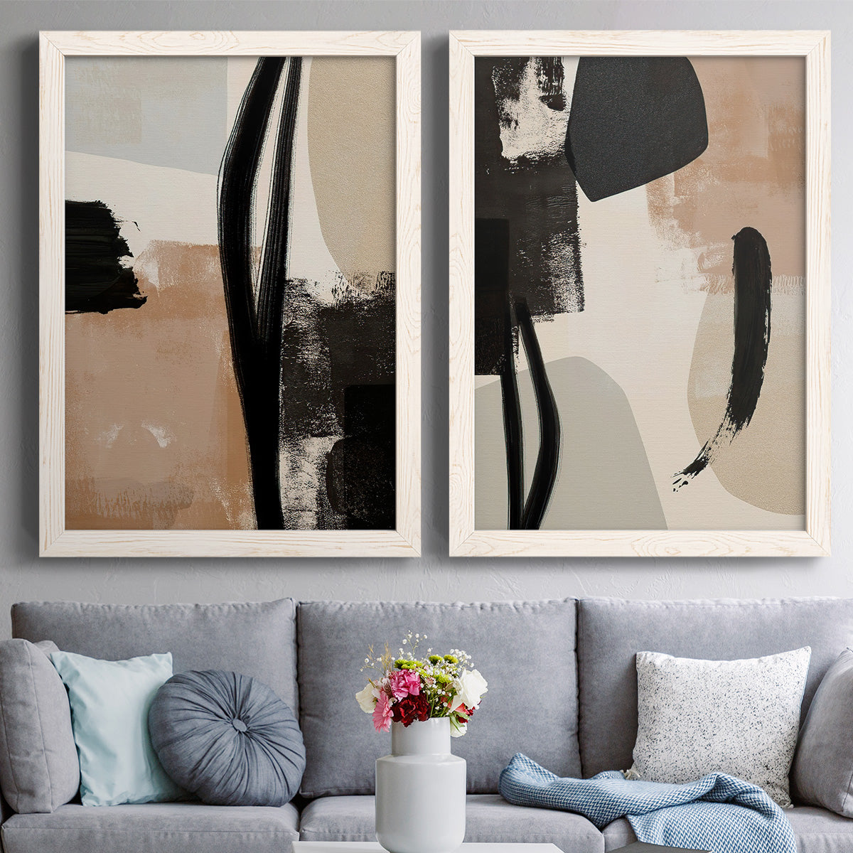 Set of two white barnwood framed canvas prints depicting paired minimalist collage-like abstracts with bold brush arcs, blocky shapes, and spacious neutral grounds above a sofa in a contemporary living room.