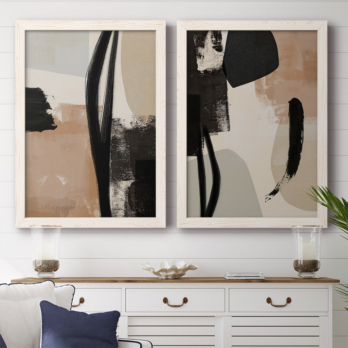 Set of two white barnwood framed canvas prints depicting a coordinated art pair of black taupe cream and beige painted forms rendered as minimalist collage-like abstracts above a dining room sideboard.