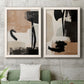 Set of two white barnwood framed canvas prints depicting a coordinated art pair of black taupe cream and beige painted forms rendered as minimalist collage-like abstracts above a sofa in a modern living room.
