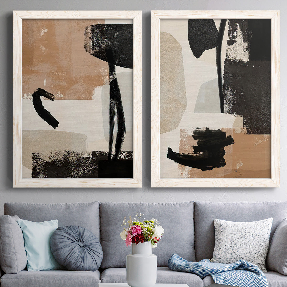 Set of two white barnwood framed canvas prints depicting paired minimalist collage-like abstracts with bold brush arcs, blocky shapes, and spacious neutral grounds above a sofa in a contemporary living room.