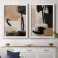 Set of two white barnwood framed canvas prints depicting a coordinated art pair of black taupe cream and beige painted forms rendered as minimalist collage-like abstracts above a dining room sideboard.