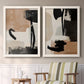 Set of two white barnwood framed canvas prints depicting two minimalist collage-like abstracts featuring black taupe cream and beige painted forms above a sideboard in a cozy sitting room.