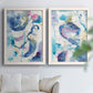 Set of two white barnwood framed canvas prints depicting looping brush marks, splatters, and translucent overlapping washes arranged across two complementary compositions above a sofa in a bright living space.