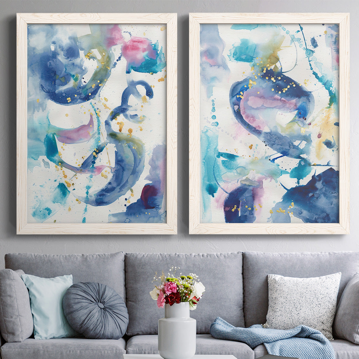 Set of two white barnwood framed canvas prints depicting paired colorful lyrical abstracts with looping brush marks, splatters, and translucent overlapping washes above a sofa in a contemporary living room.