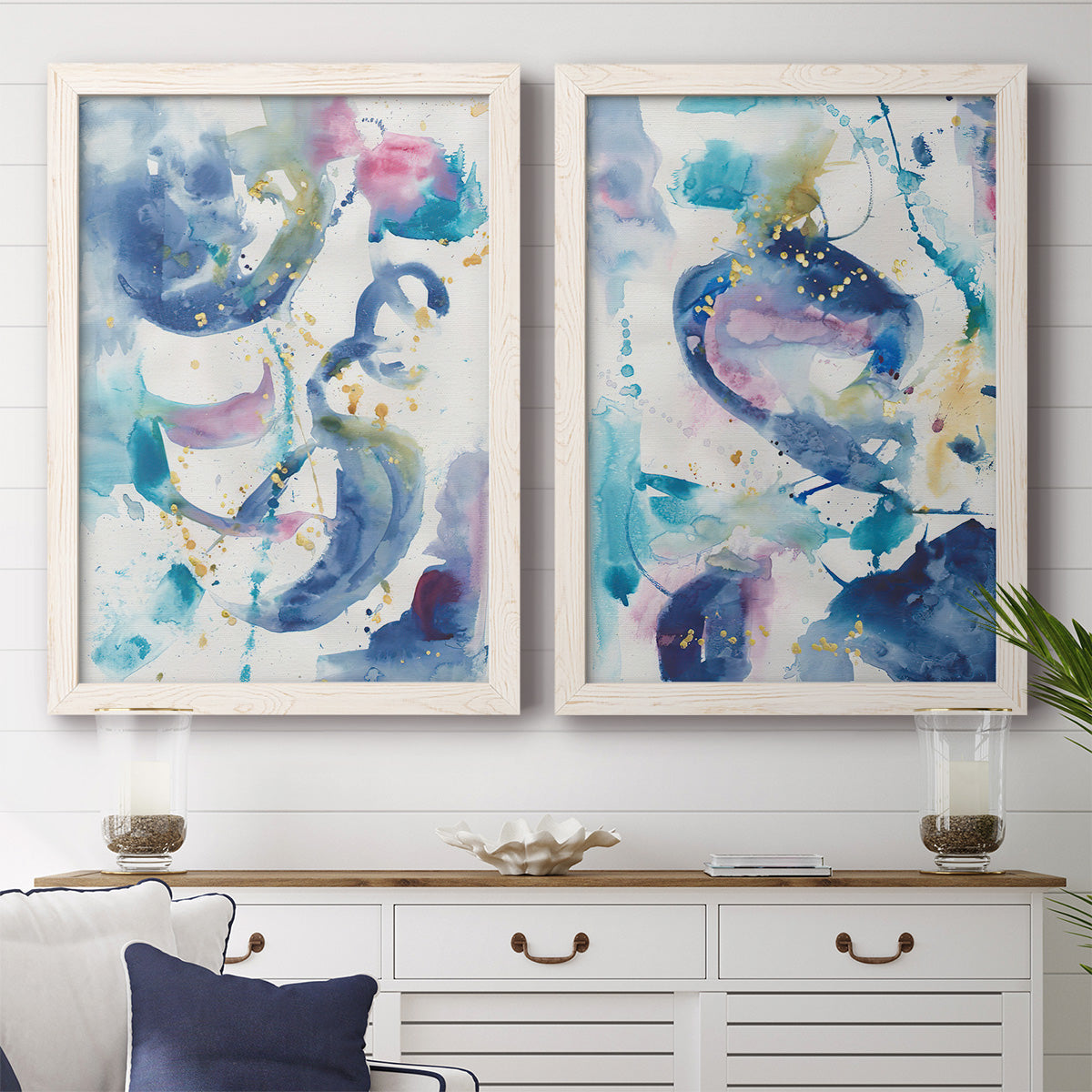 Set of two white barnwood framed canvas prints depicting a coordinated art pair of lively blue pink violet and turquoise watercolor gestures rendered as colorful lyrical abstracts above a dining room sideboard.