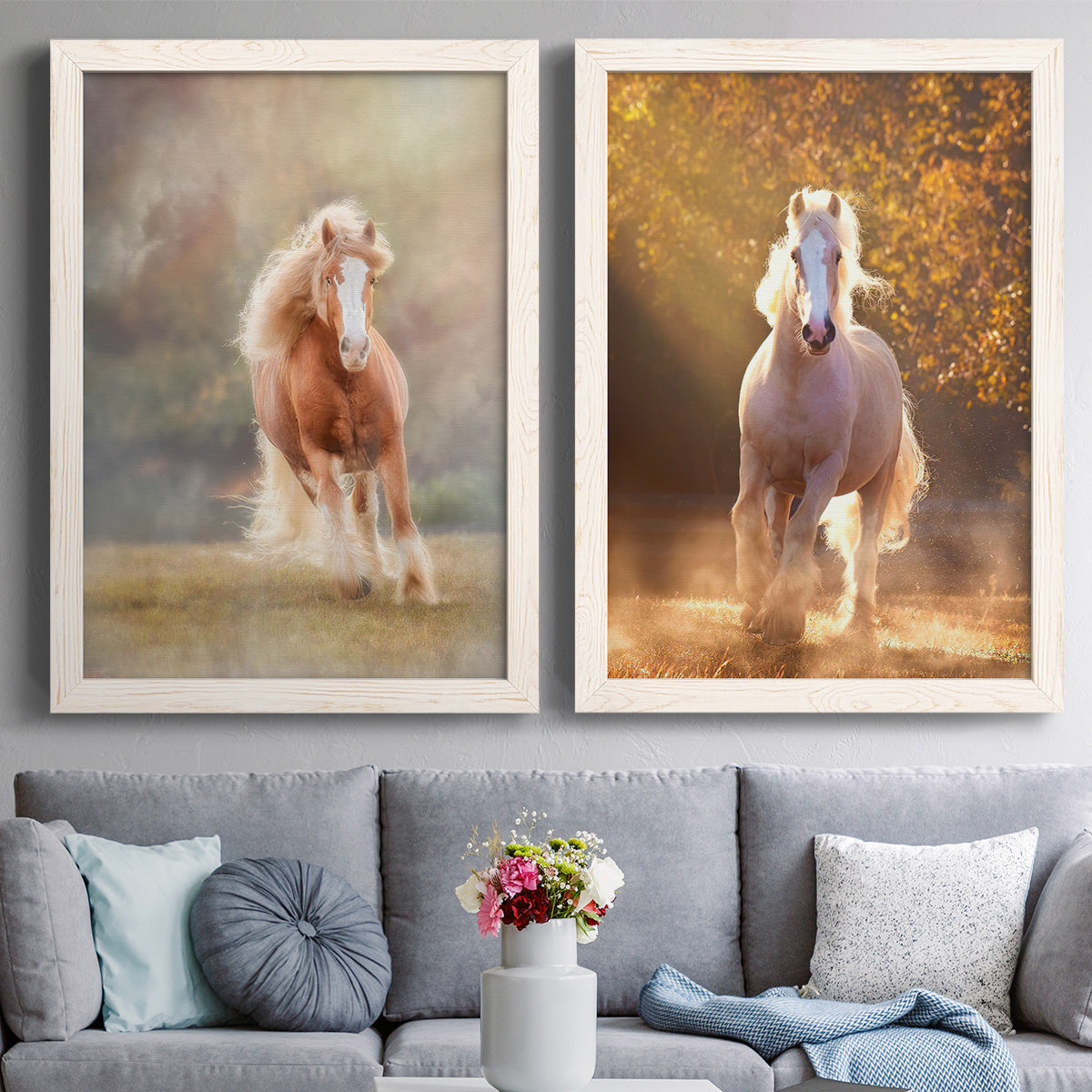 Set of two white barnwood framed canvas prints depicting paired dramatic equestrian photography with chestnut and white horses, dust, golden trees, and softly blurred backgrounds above a sofa in a contemporary living room.