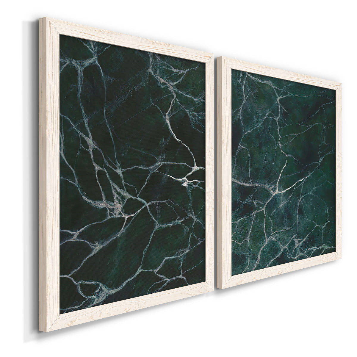 Angled view of a set of two white barnwood framed canvas prints featuring two dramatic stone-inspired abstracts featuring dark green marble veining.