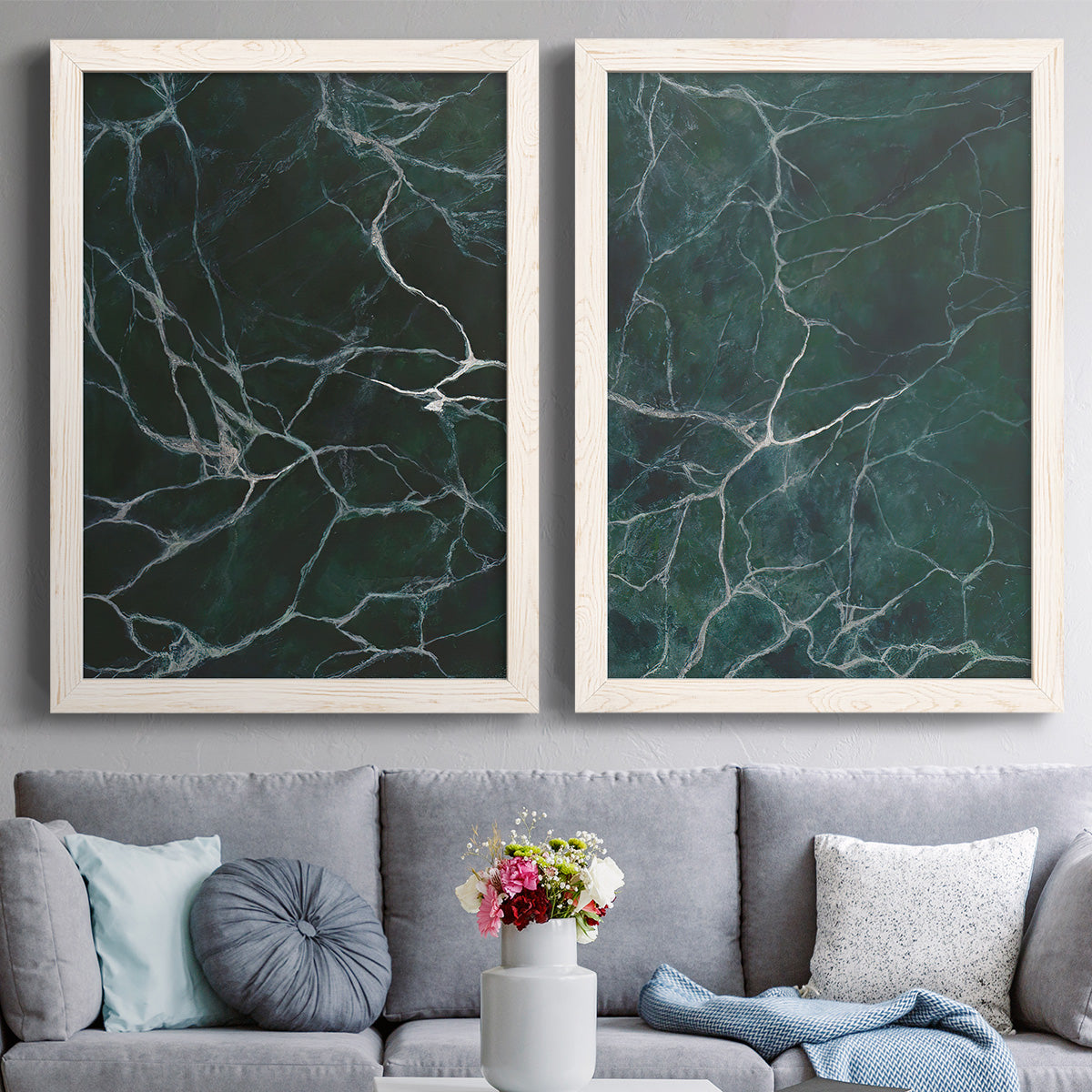 Set of two white barnwood framed canvas prints depicting paired dramatic stone-inspired abstracts with deep jade fields, fine white cracks, and glossy mineral texture above a sofa in a contemporary living room.