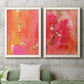 Set of two white barnwood framed canvas prints depicting a coordinated art pair of luminous coral orange and pink color fields with gold flecks rendered as glamorous fluid abstracts above a sofa in a modern living room.