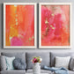 Set of two white barnwood framed canvas prints depicting paired glamorous fluid abstracts with translucent warm washes, drips, and scattered metallic accents above a sofa in a contemporary living room.