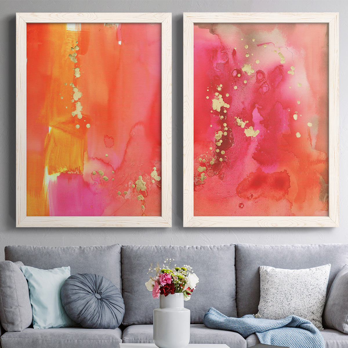 Set of two white barnwood framed canvas prints depicting paired glamorous fluid abstracts with translucent warm washes, drips, and scattered metallic accents above a sofa in a contemporary living room.