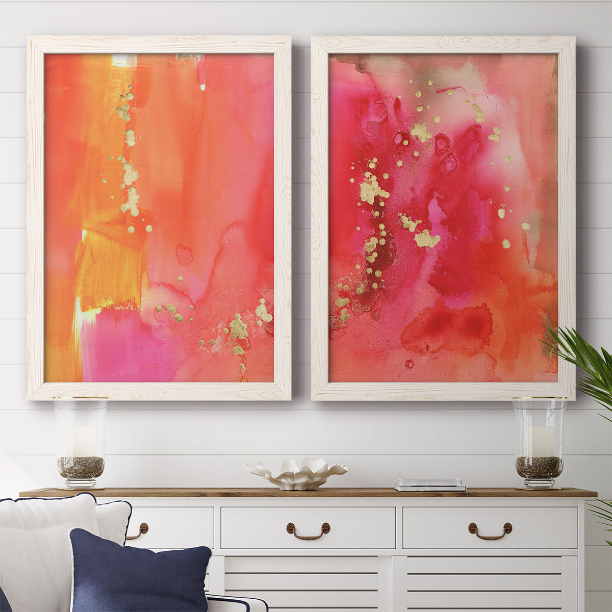 Set of two white barnwood framed canvas prints depicting a coordinated art pair of luminous coral orange and pink color fields with gold flecks rendered as glamorous fluid abstracts above a dining room sideboard.