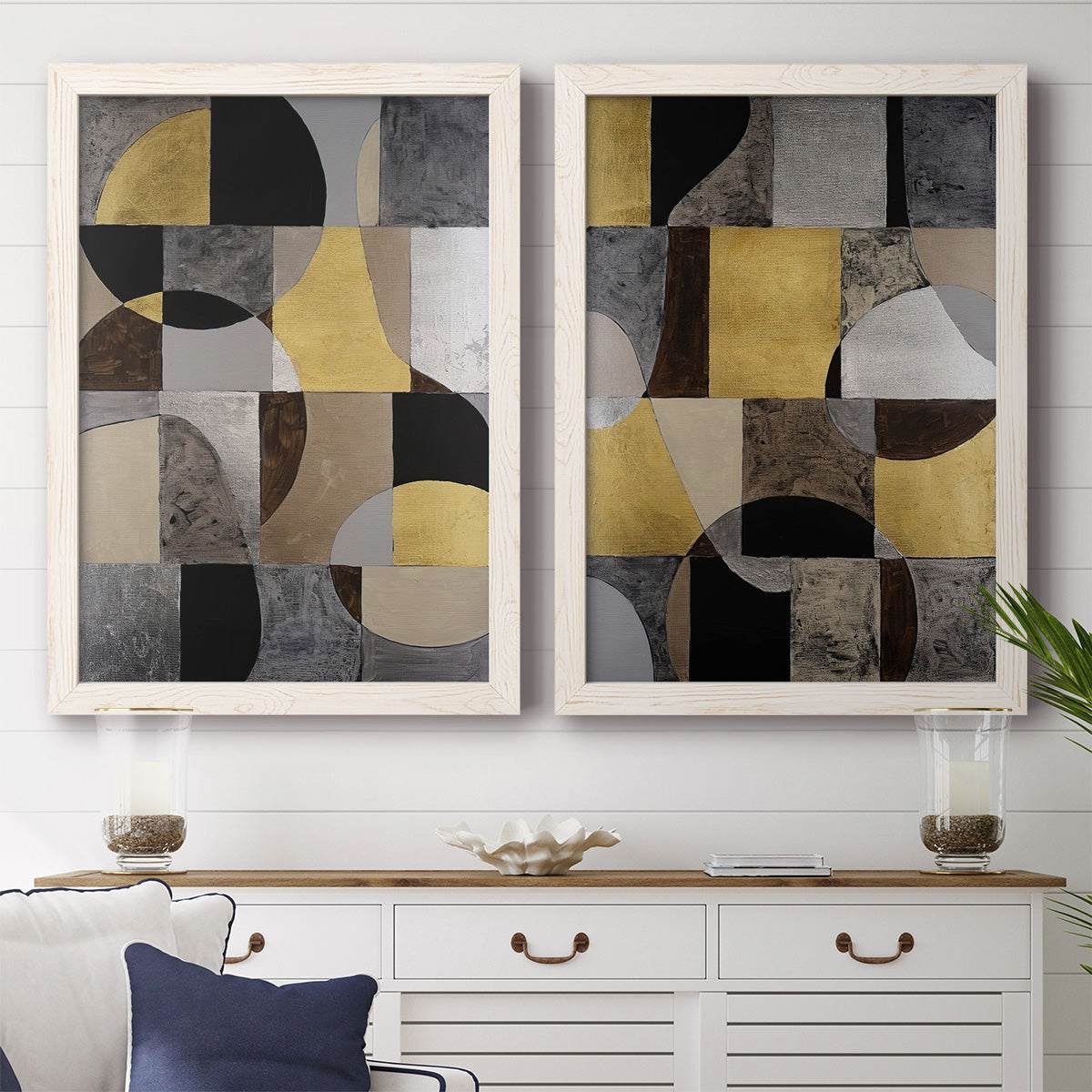 Set of two white barnwood framed canvas prints depicting a coordinated art pair of interlocking black gray cream and gold geometric sections rendered as structured modern abstracts above a dining room sideboard.