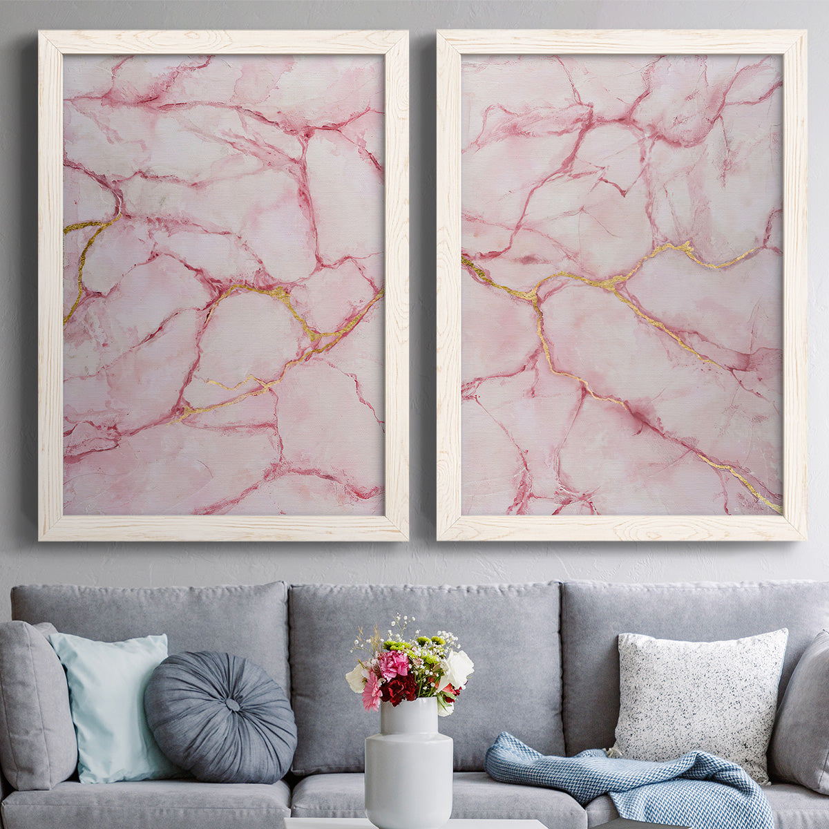 Set of two white barnwood framed canvas prints depicting paired soft stone-inspired abstracts with blush mineral clouds, branching veins, and luminous pale grounds above a sofa in a contemporary living room.