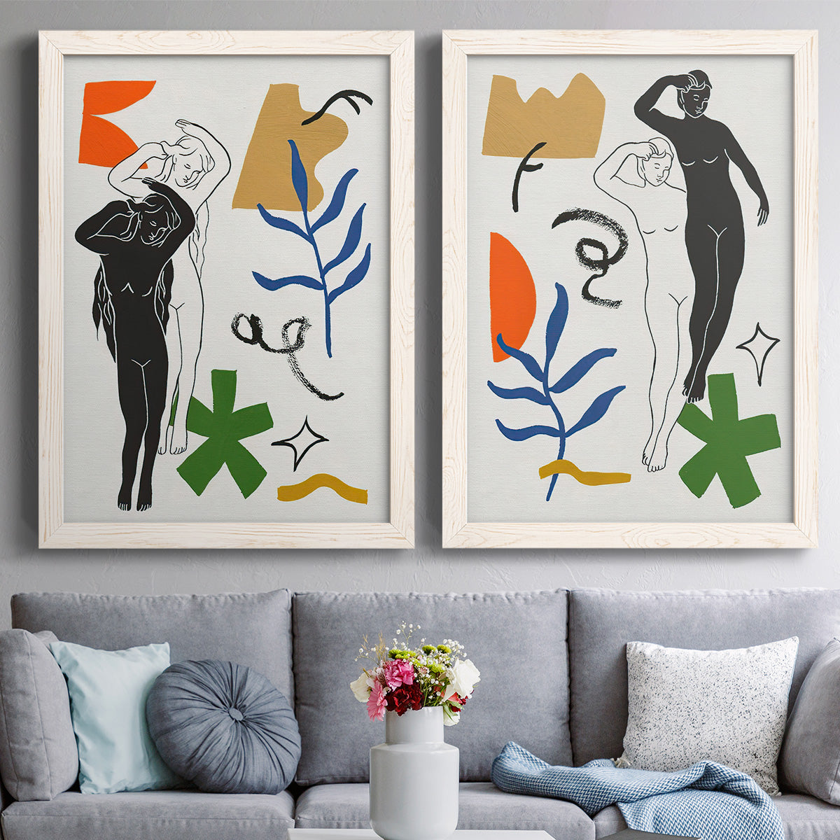 Set of two white barnwood framed canvas prints depicting expressive figure studies layered with colorful foliage celestial icons and hand drawn abstract shapes above a sofa in a contemporary living room.