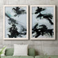 Set of two white barnwood framed canvas prints depicting a coordinated art pair of sweeping black brushstrokes over pale blue-gray fields rendered as gestural ocean-inspired abstracts above a sofa in a modern living room.