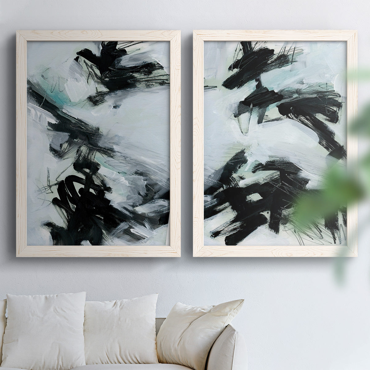 Set of two white barnwood framed canvas prints depicting bold diagonal marks, watery backgrounds, and energetic movement arranged across two complementary compositions above a sofa in a bright living space.