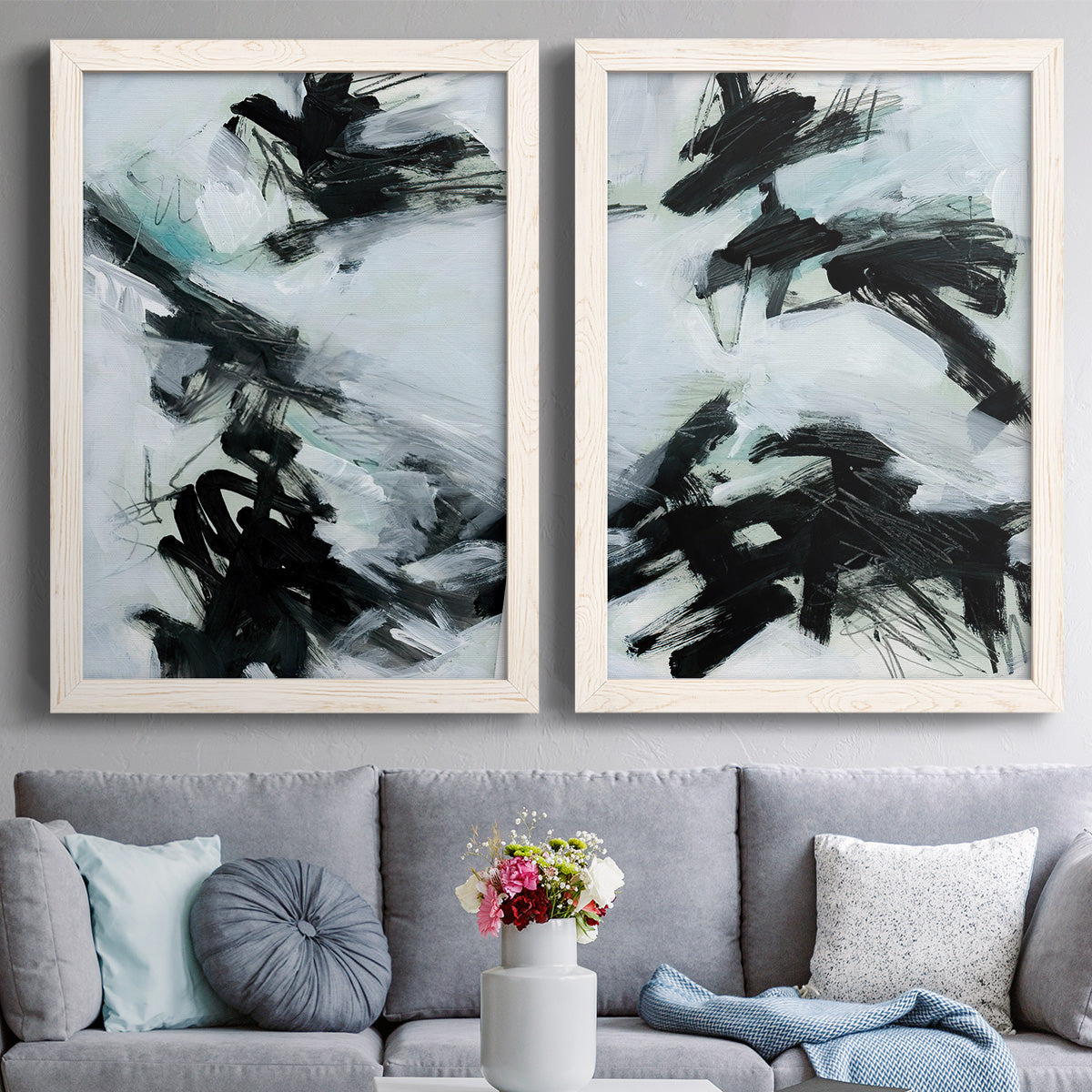 Set of two white barnwood framed canvas prints depicting paired gestural ocean-inspired abstracts with bold diagonal marks, watery backgrounds, and energetic movement above a sofa in a contemporary living room.