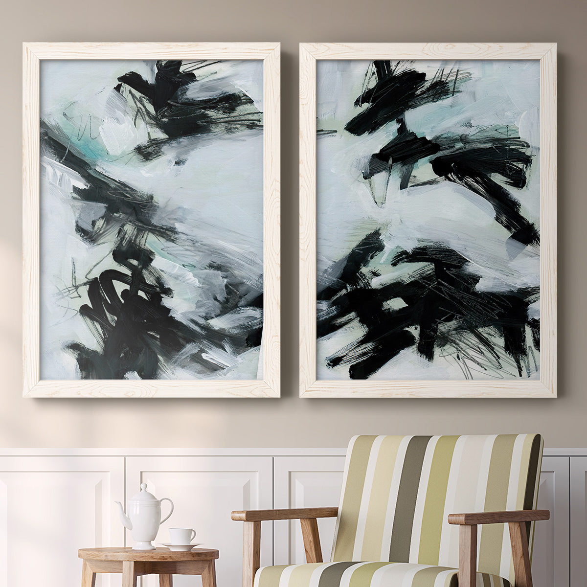 Set of two white barnwood framed canvas prints depicting two gestural ocean-inspired abstracts featuring sweeping black brushstrokes over pale blue-gray fields above a sideboard in a cozy sitting room.