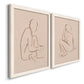 Angled view of a set of two white barnwood framed canvas prints featuring two minimalist figurative sketches featuring seated female figures drawn with single flowing lines.