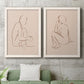 Set of two white barnwood framed canvas prints depicting a coordinated art pair of seated female figures drawn with single flowing lines rendered as minimalist figurative sketches above a sofa in a modern living room.